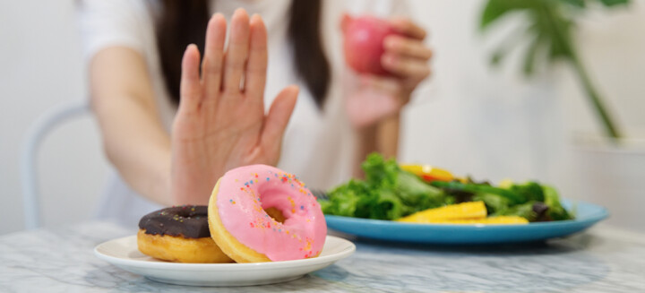 Gesunde Ernährung: Frauenhand schiebt ungesunde Donuts weg und hält gesunden Apfel